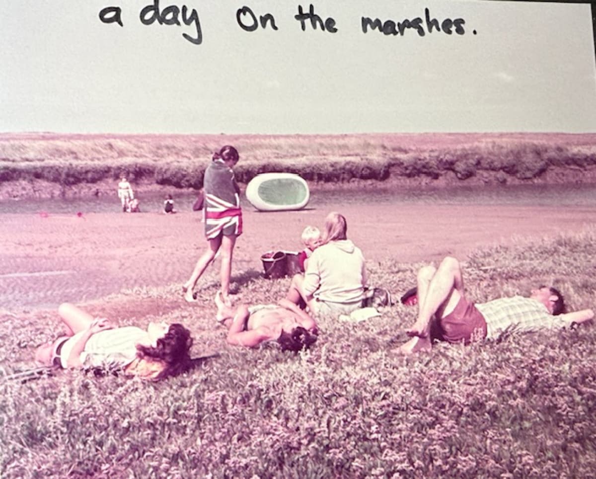 A faded photograph captioned 'a day on the marshes', showing a family relaxing by a tidal creek